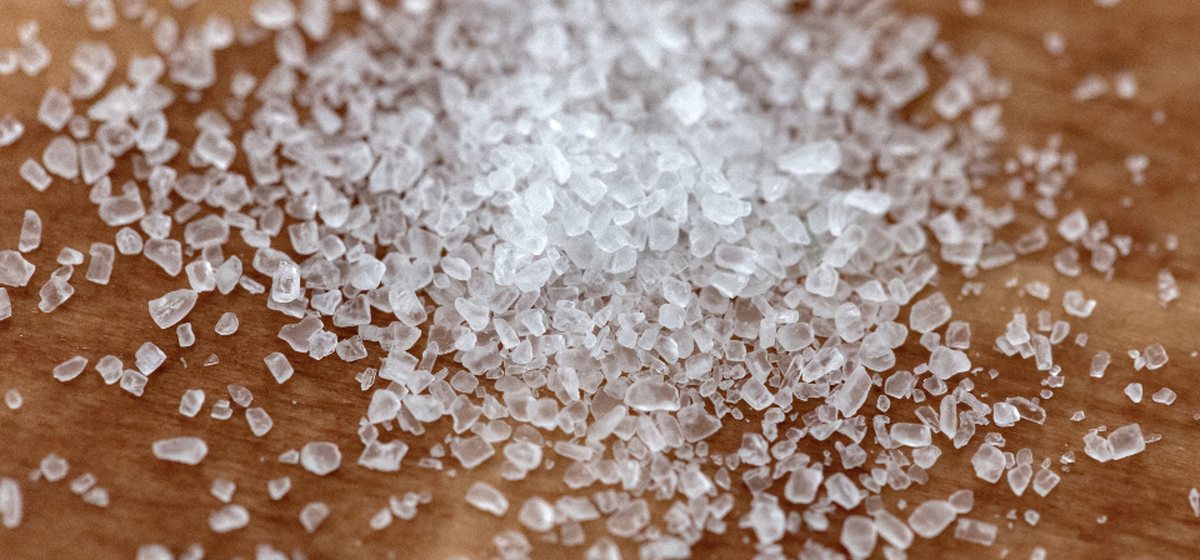 Macro photograph of coarse sea salt crystals scattered across a dark wooden surface
